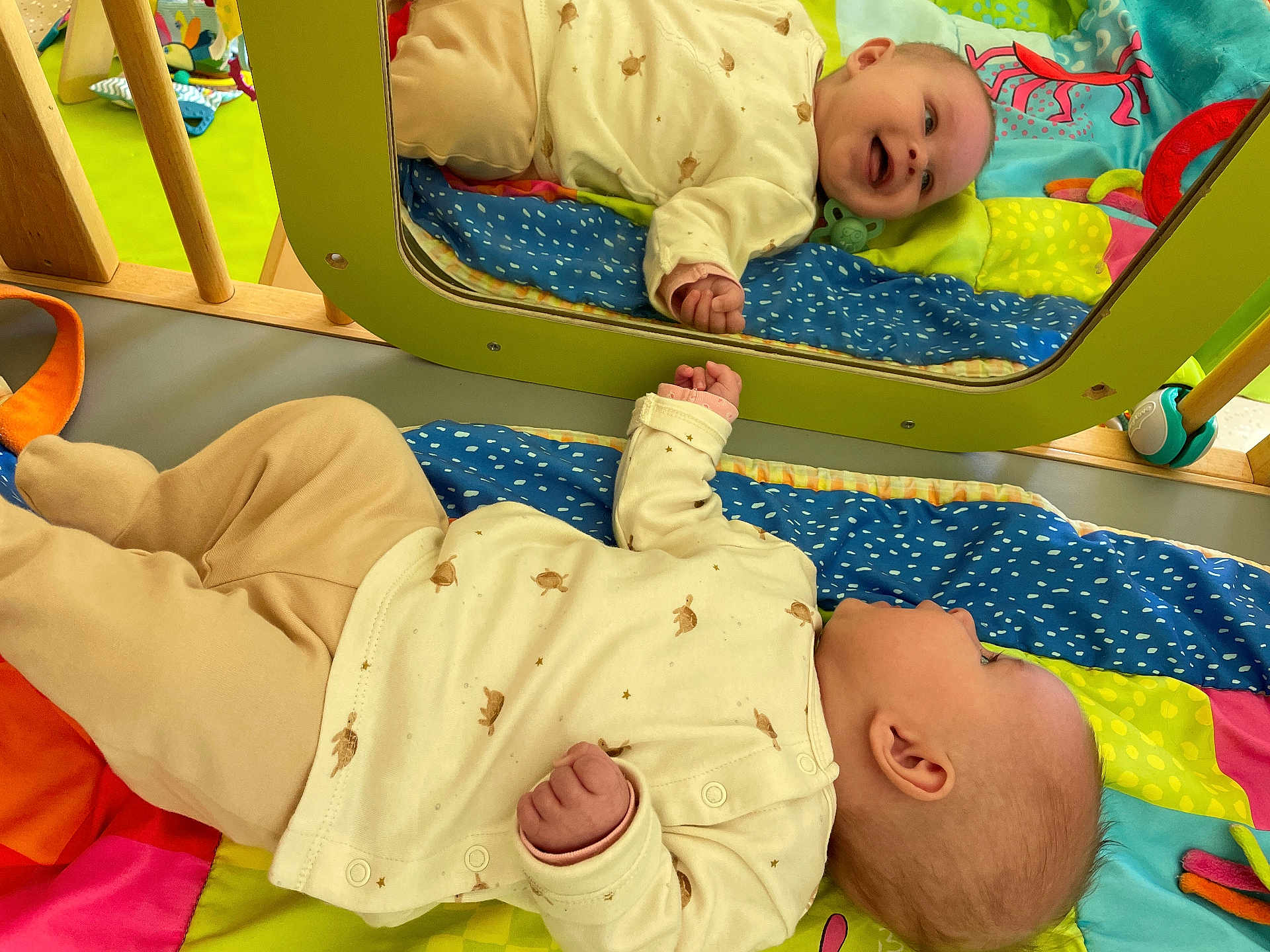 Tayssa a rejoint le concours — aidez-le/la à gagner de superbes lots ! baby, infant, mirror, reflection, play_mat, colorful, smiling, lying_down, clothing, turtle_print, wooden_frame, green_frame, happy, child, indoor, soft_toys, bright_colors, cute, casual, peaceful