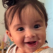 Cecilia joined the competition — help win amazing prizes! baby, child, smiling, happy, face, portrait, hair_bows, clothing, hand, fingernails, indoor, cute, infant, person, closeup, bright_eyes, joyful, orange_outfit, white_shirt, background_blur