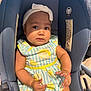 baby, child, car_seat, headband, dress, lemon_pattern, arm, hand, face, earrings, bracelet, seatbelt, blue, white, yellow, indoor, portrait, expression, clothing, person