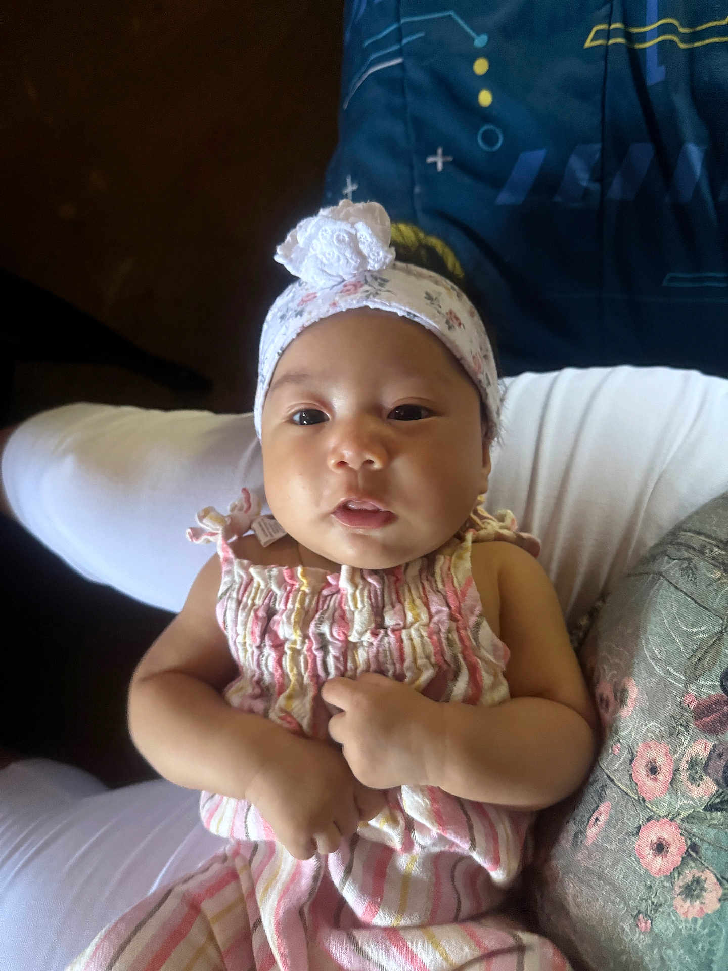 Dayana is registered to the contest to win money with this photo: baby, child, infant, headband, dress, striped_clothing, person, portrait, cute, indoors, light, hands, face, sitting, soft_light, floral_pattern, comfort, young_child, closeup, expression
