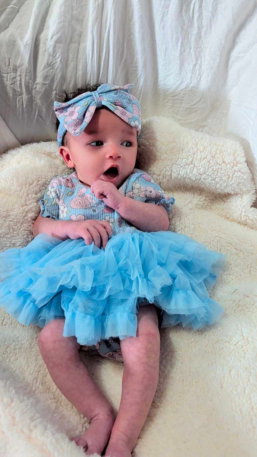 Zhuri joined the competition — help win amazing prizes! baby, infant, child, blue_tutu, headband, floral_pattern, blanket, soft_texture, curious_expression, sitting, indoors, cute, small_hands, small_feet, portrait, clothing, fabric, cozy, comfortable, skin