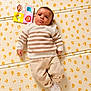 baby, infant, child, playmat, striped_sweater, beige_pants, socks, colorful_cloth, monkey, lion, rainbow, kite, floor, orange_spots, pattern, lying_down, portrait, indoor, cute, expression
