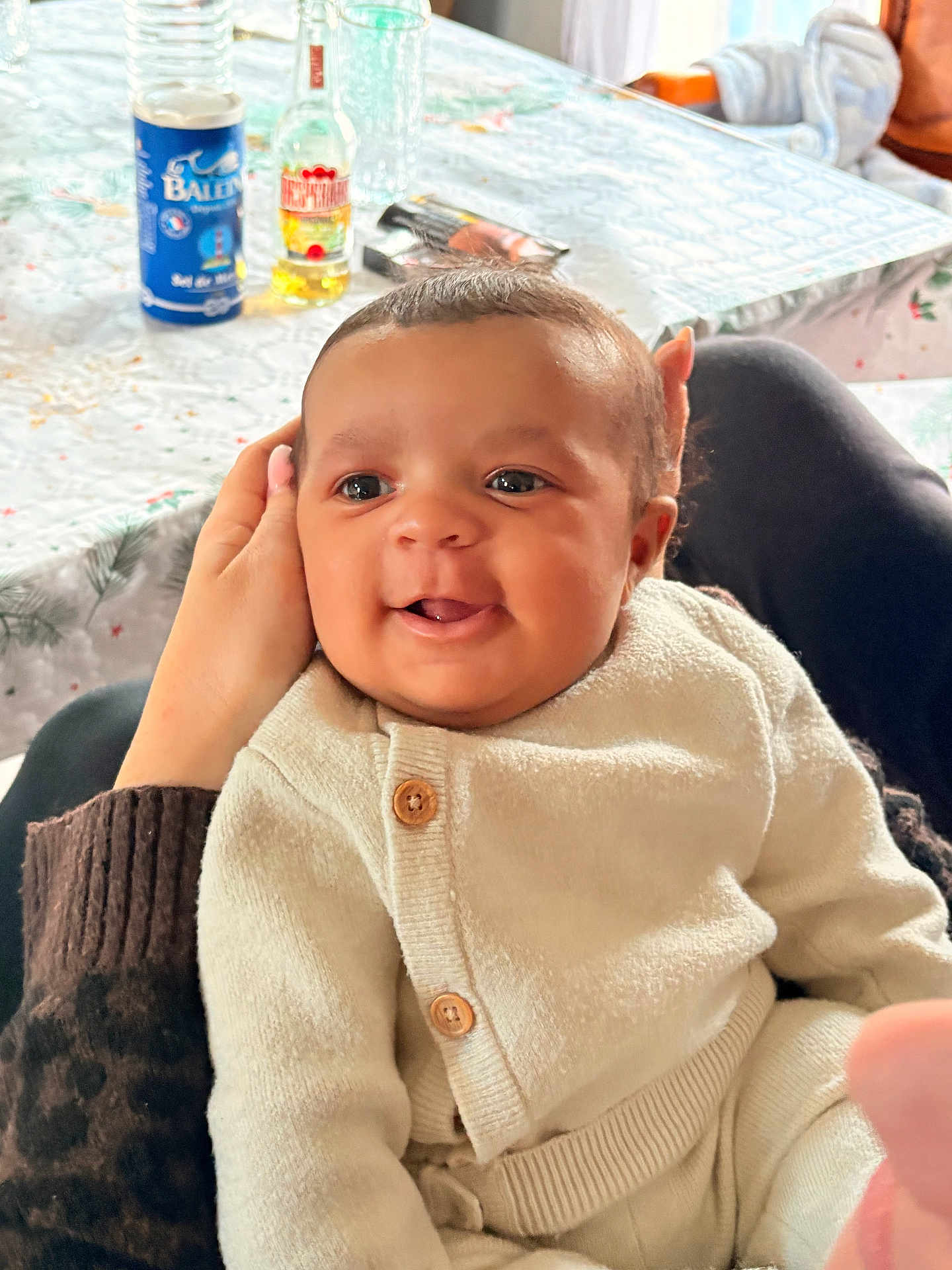 Elijah a rejoint le concours — aidez-le/la à gagner de superbes lots ! baby, infant, smile, happy, cozy, knitwear, sitting, hand, table, bottle, snack, indoor, person, face, cute, warm_clothing, holding, expression, child, portrait