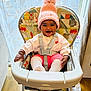 baby, high_chair, pink_hat, pom_pom, smiling, happy, indoor, child, toddler, seat_belt, colorful, toy, floor, wooden_floor, curtain, window, clothing, cute, person, cozy