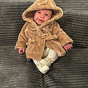 Kylo joined the competition — help win amazing prizes! baby, child, hooded_coat, smiling, sitting, couch, plush, grey, white_pants, slippers, indoor, cute, warm_clothing, happy, small_hands, portrait, cozy, infant, furniture, soft_texture