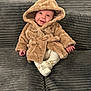 baby, child, hooded_coat, smiling, sitting, couch, plush, grey, white_pants, slippers, indoor, cute, warm_clothing, happy, small_hands, portrait, cozy, infant, furniture, soft_texture