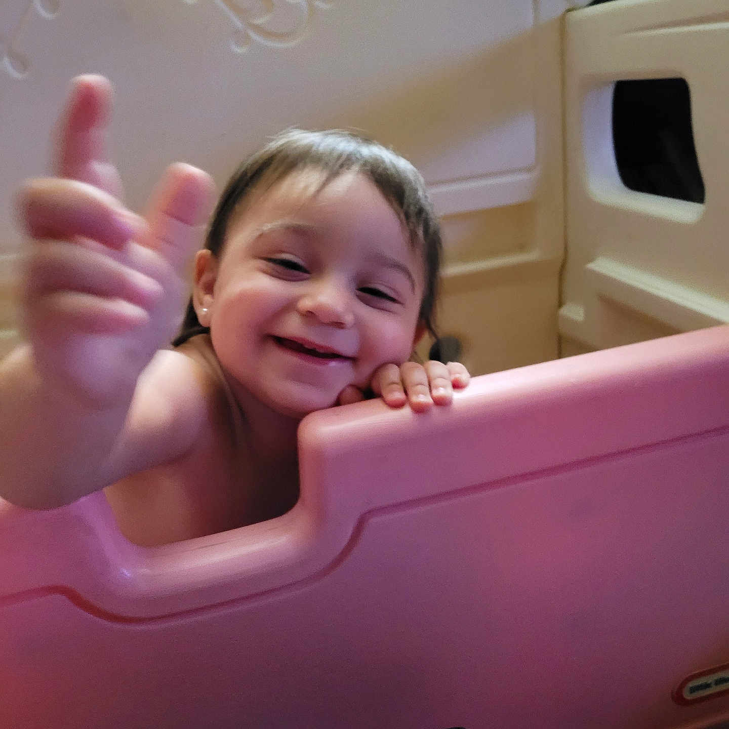 Gwendolyn is registered to the contest to win money with this photo: baby, child, closeup, curly_hair, earring, expression, face, furniture, hand, happy, indoor, infant, person, pink_barrier, playpen, room, skin, smile, toddler, toy