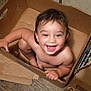 broken_box, cardboard_box, child, cute, face, floor, hair, happy, home, indoor, joy, person, playful, sitting, skin, smiling, snack_box, toddler, wooden_floor, young_child