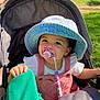 baby, child, clothing, cute, daytime, grass, green_cloth, happy, hat, infant, nature, outdoor, pacifier, person, pink_overalls, portrait, stroller, summer, sunlight, toddler