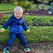 Mattéo participe au concours pour gagner de l'argent avec cette photo : child, toddler, smiling, blue_jacket, blonde_hair, outdoor, garden, grass, plants, greenery, casual_clothing, shoes, sitting, happy, nature, daylight, cute, face, portrait, playful