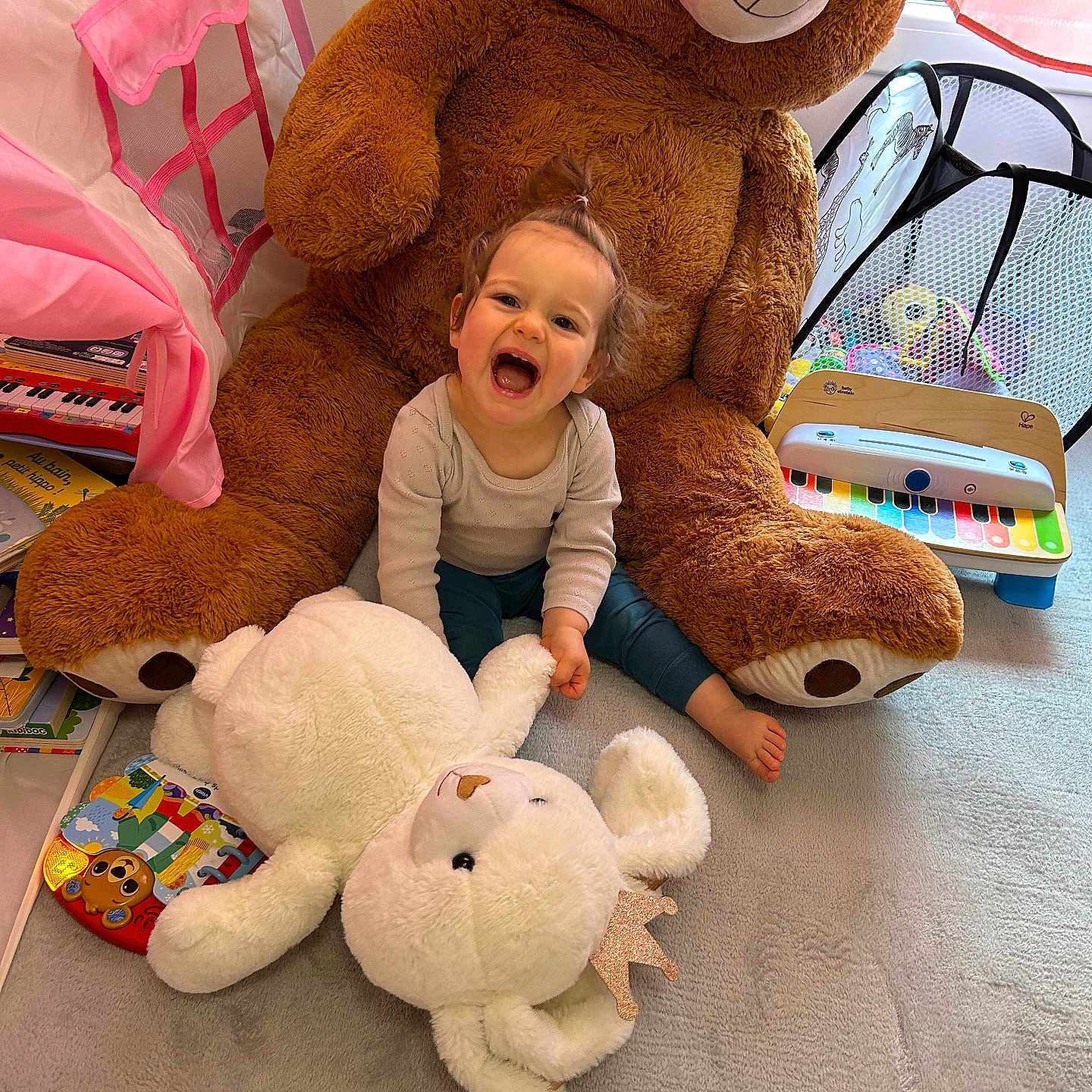 Lou a rejoint le concours — aidez-le/la à gagner de superbes lots ! toddler, child, teddy_bear, stuffed_animal, toy, playroom, piano, book, carpet, curtain, window, laughing, happy, indoor, person, plush, baby, smiling, floor, cozy