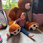 Lou a rejoint le concours — aidez-le/la à gagner de superbes lots ! toddler, child, plush_toy, teddy_bear, carpet, window, indoor, smile, happy, toy_storage, storage_box, play_area, childrens_room, footwear_absent, casual_clothing, natural_light, home, cute, furniture, person