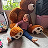 toddler, child, plush_toy, teddy_bear, carpet, window, indoor, smile, happy, toy_storage, storage_box, play_area, childrens_room, footwear_absent, casual_clothing, natural_light, home, cute, furniture, person