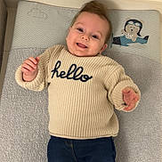 Lou a rejoint le concours — aidez-le/la à gagner de superbes lots ! baby, child, clothing, cozy, cute, face, hair, happy, hello_text, indoor, infant, jeans, lying_down, person, portrait, smiling, soft_mat, sweater, toddler, warm