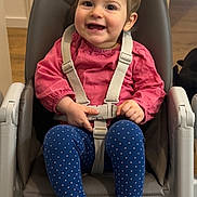 Lou participe au concours pour gagner de l'argent avec cette photo : child, toddler, baby, high_chair, smile, happy, straps, buckle, polka_dot, leggings, barefoot, toes, pink_top, indoor, wood_floor, portrait, seat, hair_clip, hands, feeding_chair