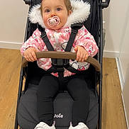Lou participe au concours pour gagner de l'argent avec cette photo : baby, stroller, pacifier, pink_jacket, fur_hood, harness, shoes, sneakers, wooden_floor, indoor, toddler, seat, bumper_bar, portrait, playful, cute, eyes, hands, clothing, pram