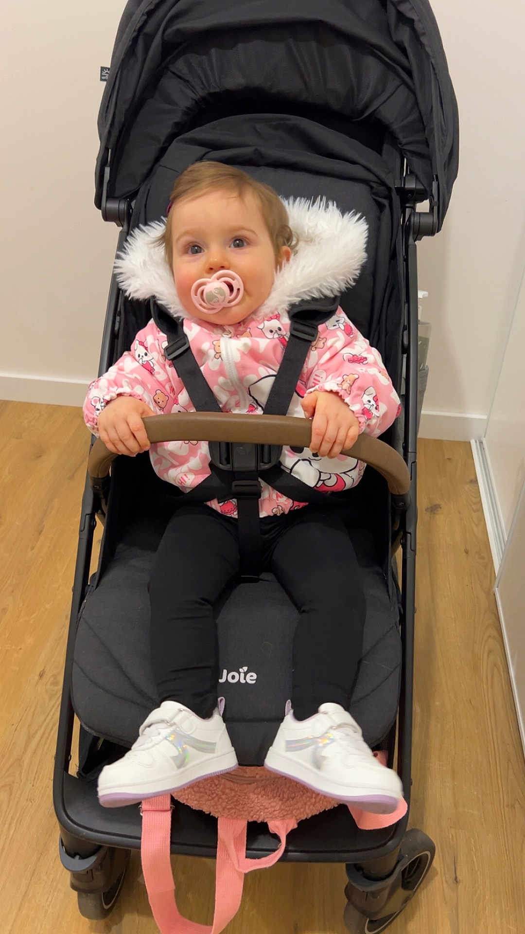Lou participe au concours pour gagner de l'argent avec cette photo : baby, stroller, pacifier, pink_jacket, fur_hood, harness, shoes, sneakers, wooden_floor, indoor, toddler, seat, bumper_bar, portrait, playful, cute, eyes, hands, clothing, pram
