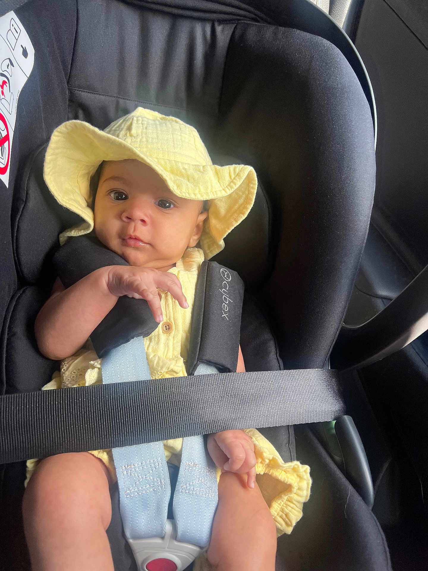 Kiana is registered to the contest to win money with this photo: baby, car_seat, yellow_hat, yellow_clothing, infant, child, seatbelt, car_interior, safety, straps, cute, portrait, looking_at_camera, small_hands, soft_light, black_seat, child_safety, hat, infant_clothing, car_trip