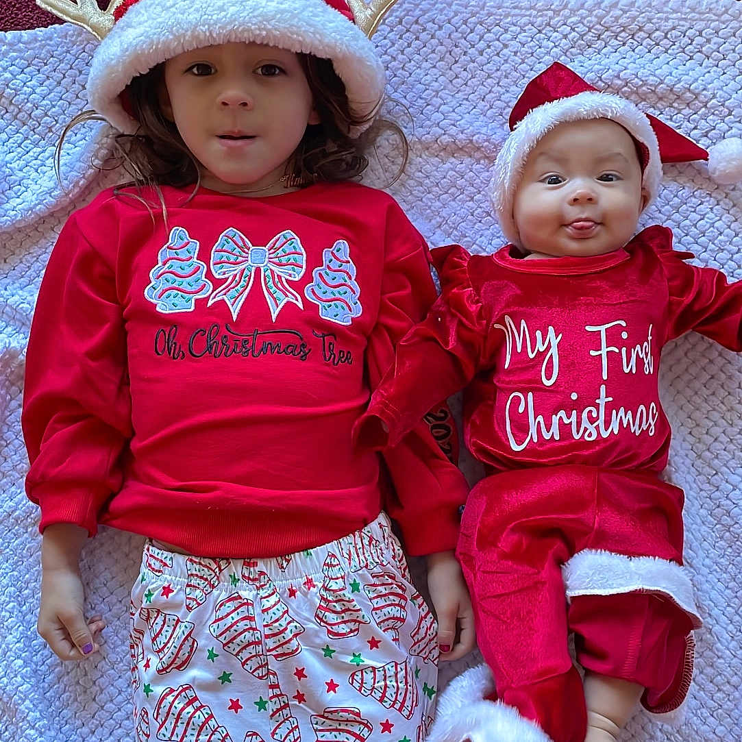 Kahoku is registered to the contest to win money with this photo: baby, blanket, child, christmas, cute, family, festive, happy, hat, holiday, indoors, lying_down, pajamas, patterned_pants, red_clothing, reindeer_ears, smiling, socks, tongue_out, white_trim