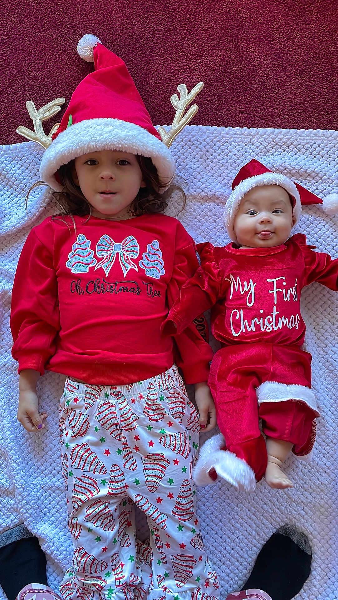 Kahoku is registered to the contest to win money with this photo: child, baby, christmas, holiday, pajamas, hat, reindeer_ears, blanket, smiling, tongue_out, cute, festive, red_clothing, white_trim, lying_down, indoors, socks, patterned_pants, happy, family