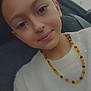 child, girl, face, smile, necklace, amber_beads, white_sweater, portrait, car_seat, seatbelt, indoor, closeup, young, casual, cute, happy, head, hair, person, emoji