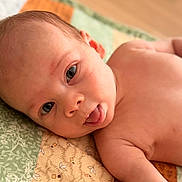 Jonah is registered to the contest to win money with this photo: baby, infant, tongue_out, lying_down, patchwork_quilt, skin, face, eyes, expression, cute, child, playful, young, indoors, closeup, head, shoulder, newborn, soft_light, portrait