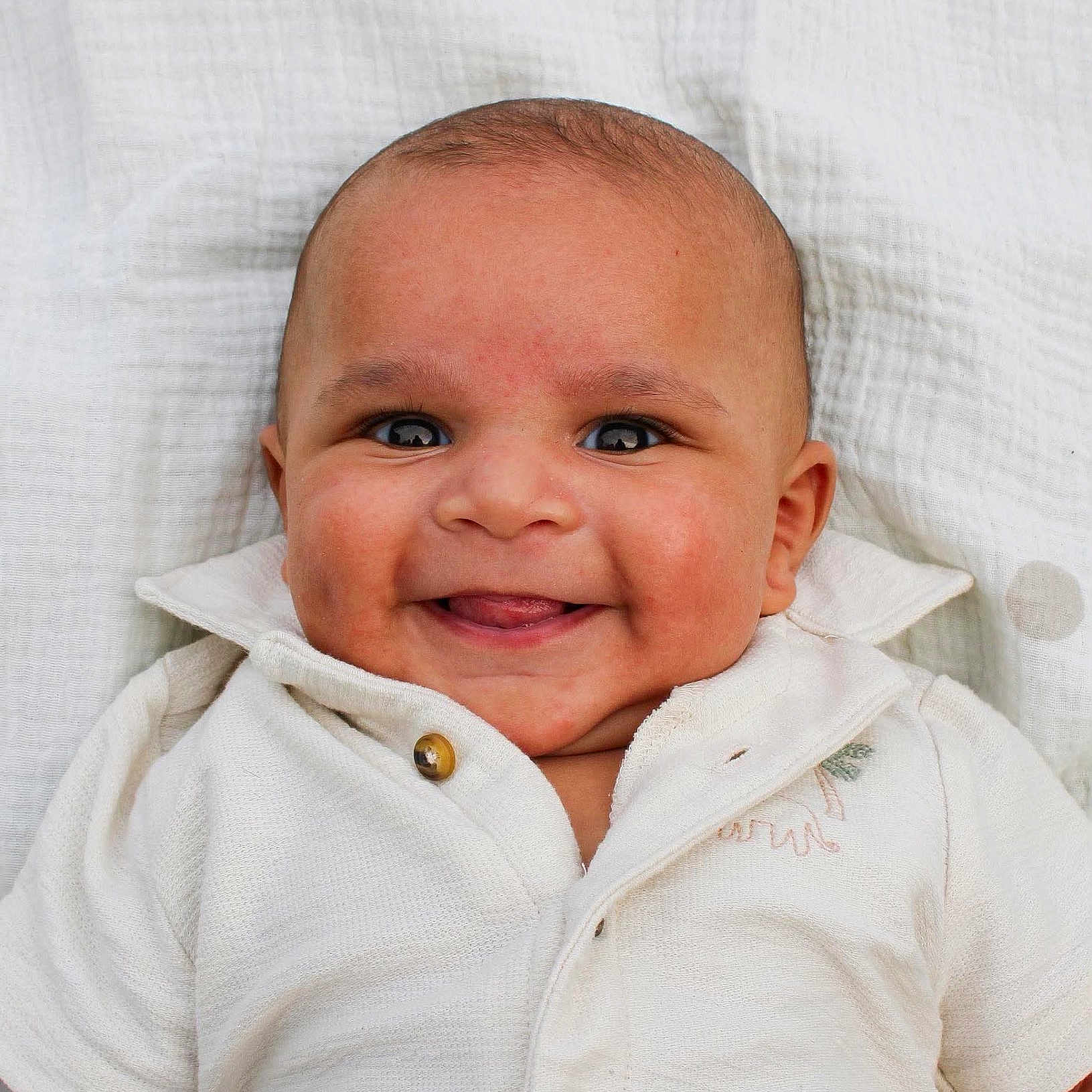 Malic is registered to the contest to win money with this photo: baby, infant, child, smiling, portrait, face, eyes, tongue, happy, white_clothing, onesie, button, blanket, fabric, indoor, close_up, head, adorable, lying_down, photography
