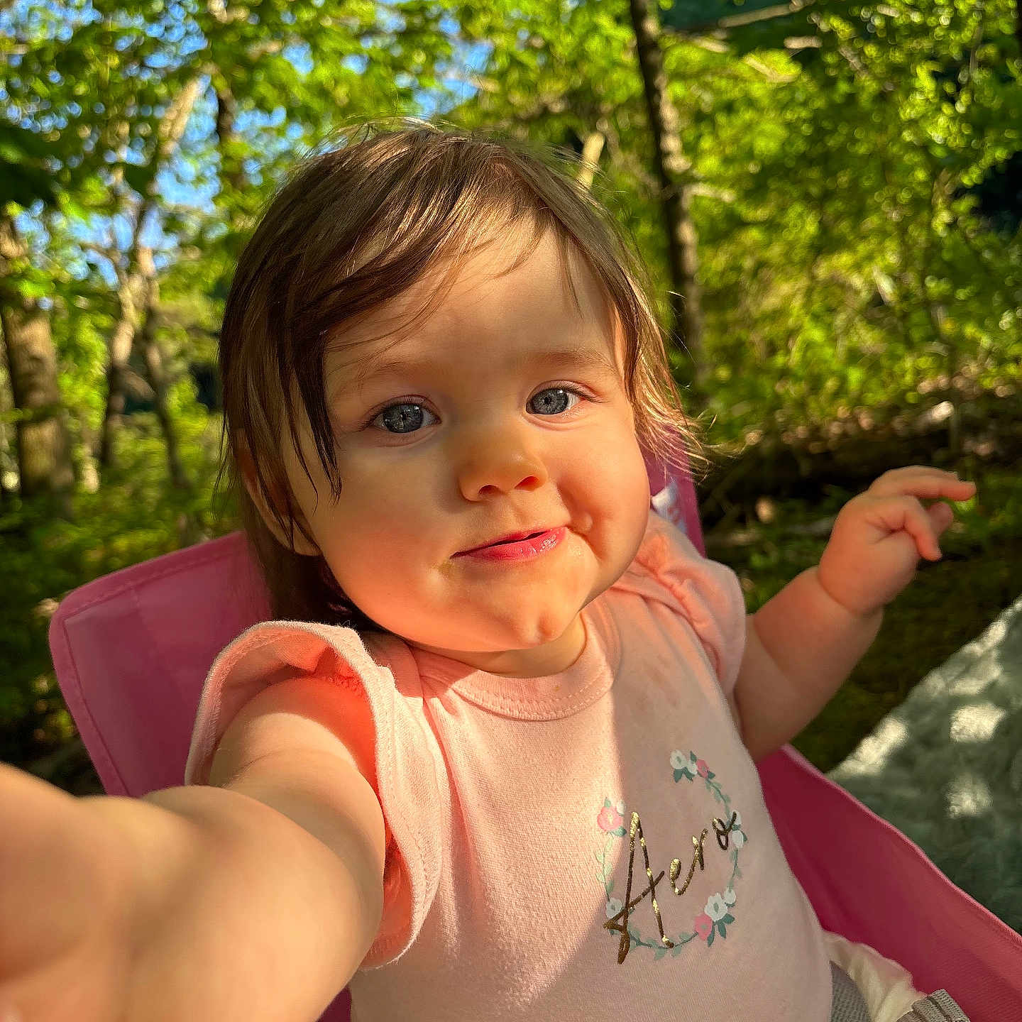 Isabella is registered to the contest to win money with this photo: toddler, child, selfie, outdoor, nature, trees, greenery, sunlight, pink_chair, smile, face, cute, baby, summer, daylight, happy, person, clothing, shirt, portrait