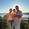 Isabella is registered to the contest to win money with this photo: family, baby, woman, man, outdoor, sunset, river, balcony, fence, locks, smile, casual_clothing, nature, scenic_view, portrait, happy, people, holding_baby, blue_sky, jeans