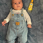Eitan Medina joined the competition — help win amazing prizes! baby, infant, denim_overalls, teddy_bear_patch, blanket, dinosaur_pattern, bottle, chamomile_spray, laying_down, curious_expression, clothing, footwear_absent, hand, face, head, skin, indoors, floor, soft_texture, cute