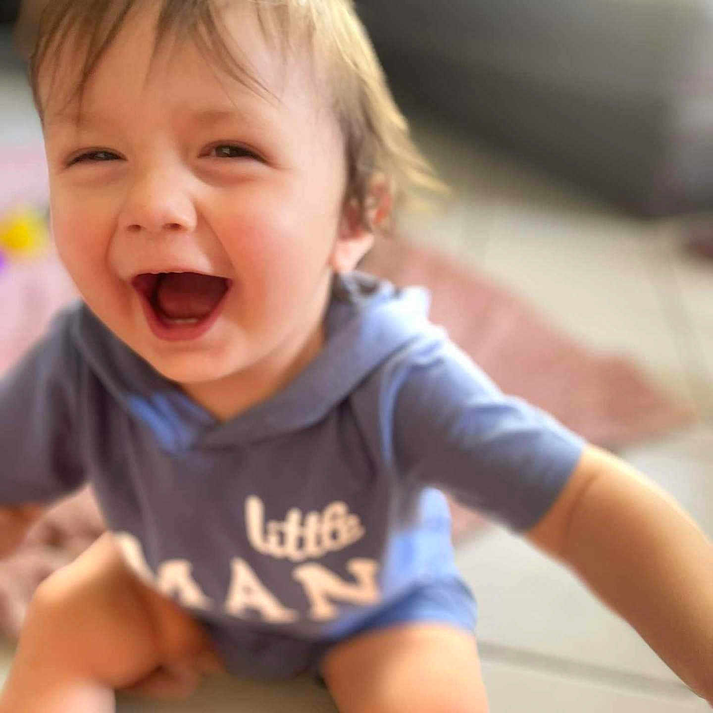 Gabriel a rejoint le concours — aidez-le/la à gagner de superbes lots ! baby, blue_hoodie, blurry_background, casual_clothing, child, closeup, cute, expression, face, floor, happy, indoor, joyful, laughing, person, playful, sitting, smiling, toddler, young_child