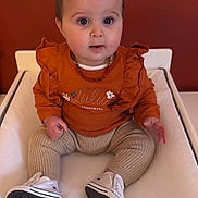 Adeilia a rejoint le concours — aidez-le/la à gagner de superbes lots ! baby, child, infant, sitting, clothing, orange_top, ruffles, pants, beige, white_shoes, sneakers, hair_clip, flower, drool, indoor, changing_pad, face, cute, portrait, person