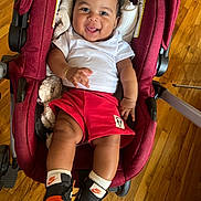 Suriel is registered to the contest to win money with this photo: baby, stroller, red, smiling, white_shirt, red_shorts, mickey_patch, nike_sneakers, wooden_floor, happy, infant, footwear, person, cute, indoors, child, sitting, fashion, casual_clothing, playful