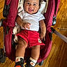 baby, stroller, red, smiling, white_shirt, red_shorts, mickey_patch, nike_sneakers, wooden_floor, happy, infant, footwear, person, cute, indoors, child, sitting, fashion, casual_clothing, playful