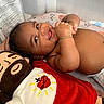 baby, smiling, infant, plush_toy, doll, bracelet, diaper, playpen, blanket, pattern, happy, cute, child, indoors, lying_down, skin, face, hand, toy, cozy