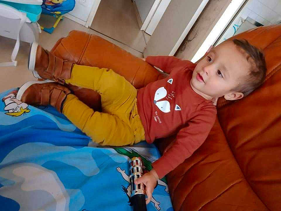 Ylias participe au concours pour gagner de l'argent avec cette photo : baby, baby_toddler_clothing, child, comfort, couch, electric_blue, fun, human_leg, lap, leisure, linens, orange, person, pillow, play, room, sitting, smile, textile, thigh