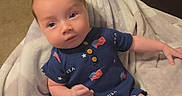 Levi is registered to the contest to win money with this photo: baby, blanket, blue_clothing, book, bookshelf, carpet, child, cute, face, feet, furniture, hand, indoor, infant, person, relaxing, romper, soft, usa_flag, young