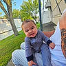 baby, child, striped_onesie, outdoor, grass, tree, person, tattoo, adult, lawn, mobile_home, sunny, sidewalk, blue_sky, smiling, cute, face, hand, footed_pajamas, casual