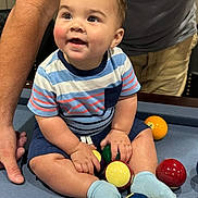 Johdi joined the competition — help win amazing prizes! toddler, child, pool_table, billiard_balls, blue_socks, striped_shirt, shorts, indoor, smiling, person, adult_arm, playing, colorful, seated, fun, curious, happy, game_room, family, support
