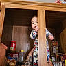baby, child, pajamas, pantry, wooden_cabinet, snacks, tattoo, adult_hand, food_items, curious, peek, indoor, shelf, bread, peanut_butter, instant_noodles, person, holding, cute, playful