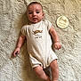 baby, infant, child, onesie, plush_rug, milestone_marker, four_months, wooden_plaque, cute, smiling, lying_down, soft_texture, beige, portrait, indoor, baby_clothing, face, hand, foot, milestone