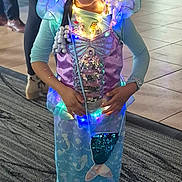 Ry'Onna joined the competition — help win amazing prizes! child, girl, mermaid_costume, lights, smiling, braids, indoor, carpet, floor, people, costume, purple, blue, long_sleeves, happy, portrait, holiday, celebration, standing, decorative_lights