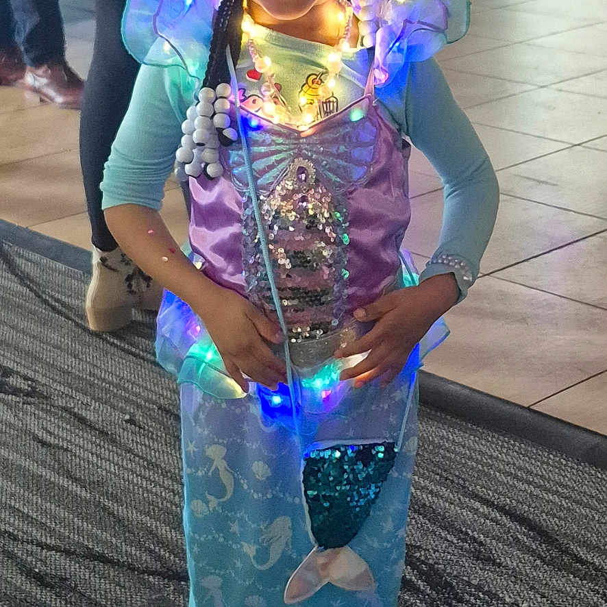 Ry'Onna joined the competition — help win amazing prizes! child, girl, mermaid_costume, lights, smiling, braids, indoor, carpet, floor, people, costume, purple, blue, long_sleeves, happy, portrait, holiday, celebration, standing, decorative_lights