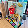 advertisement, burger_king, cartoon, casual_clothing, child, colorful, daylight, decor, door, floor_mat, girl, glasses, indoor, minions, playful_pose, red_sweater, smile, unicorn, window, wooden_floor