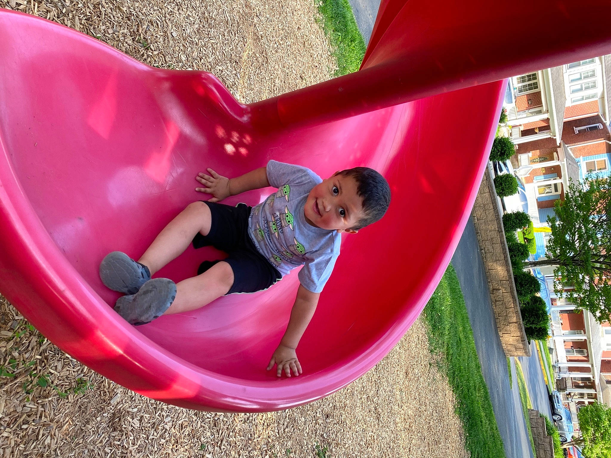 Lyam is registered to the contest to win money with this photo: building, child, chute, city, fun, grass, inflatable, leg, leisure, magenta, outdoor_play_equipment, person, pink, plant, playground, playground_slide, recreation, summer, toddler, tree