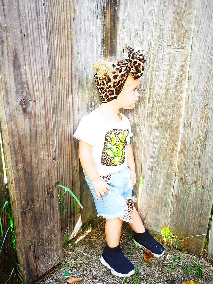 Trinity is registered to the contest to win money with this photo: beanie, cap, child, fawn, glasses, grass, headgear, pattern, person, photography, plant, shoe, t_shirt, toddler, tree, wood, yellow