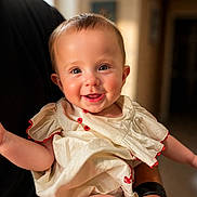 Selena joined the competition — help win amazing prizes! baby, smiling, child, face, happy, person, portrait, indoor, clothing, red_buttons, skin, hand, adult_hand, watch, black_shirt, cute, infant, warm_lighting, closeup, joy