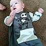 baby, infant, carpet, clothing, gray_outfit, skeleton_print, ghost_print, hand_motion, lying_down, curious_expression, blue_eyes, indoor, child, cute, soft_lighting, carpet_texture, small_person, toddler, onesie, baby_garment