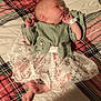 newborn, baby, sleeping, plaid_blanket, green_top, lace_skirt, infant, bed, soft_fabric, cute, peaceful, lying_down, cozy, indoors, person, small_hands, small_feet, wrapped, resting, child