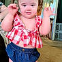 toddler, child, indoor, pigtails, red_checkered_top, denim_shorts, carpet, living_room, ceiling_fan, furniture, person, smiling, cute, young_child, playful, home, portrait, standing, baby, casual